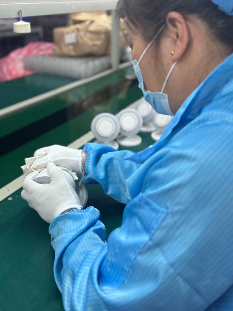 Factory worker wearing white gloves performing final surface cleaning and polishing on wireless chargers to ensure pristine condition.