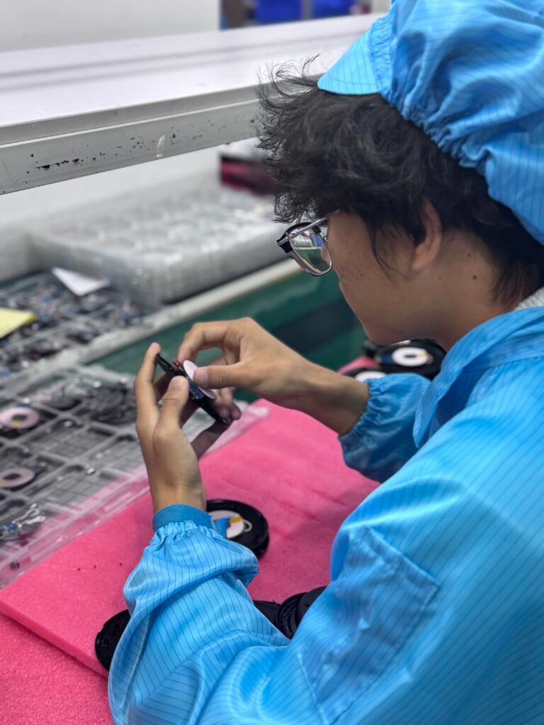 Factory worker assembling magnetic induction coils for Qi-standard wireless chargers on the production line.
