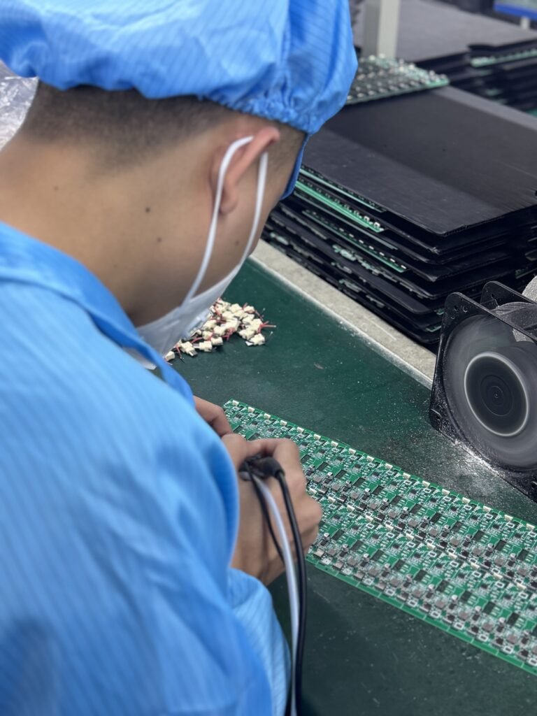 Skilled factory worker performing precision manual soldering on wireless charger circuit boards (PCBA).